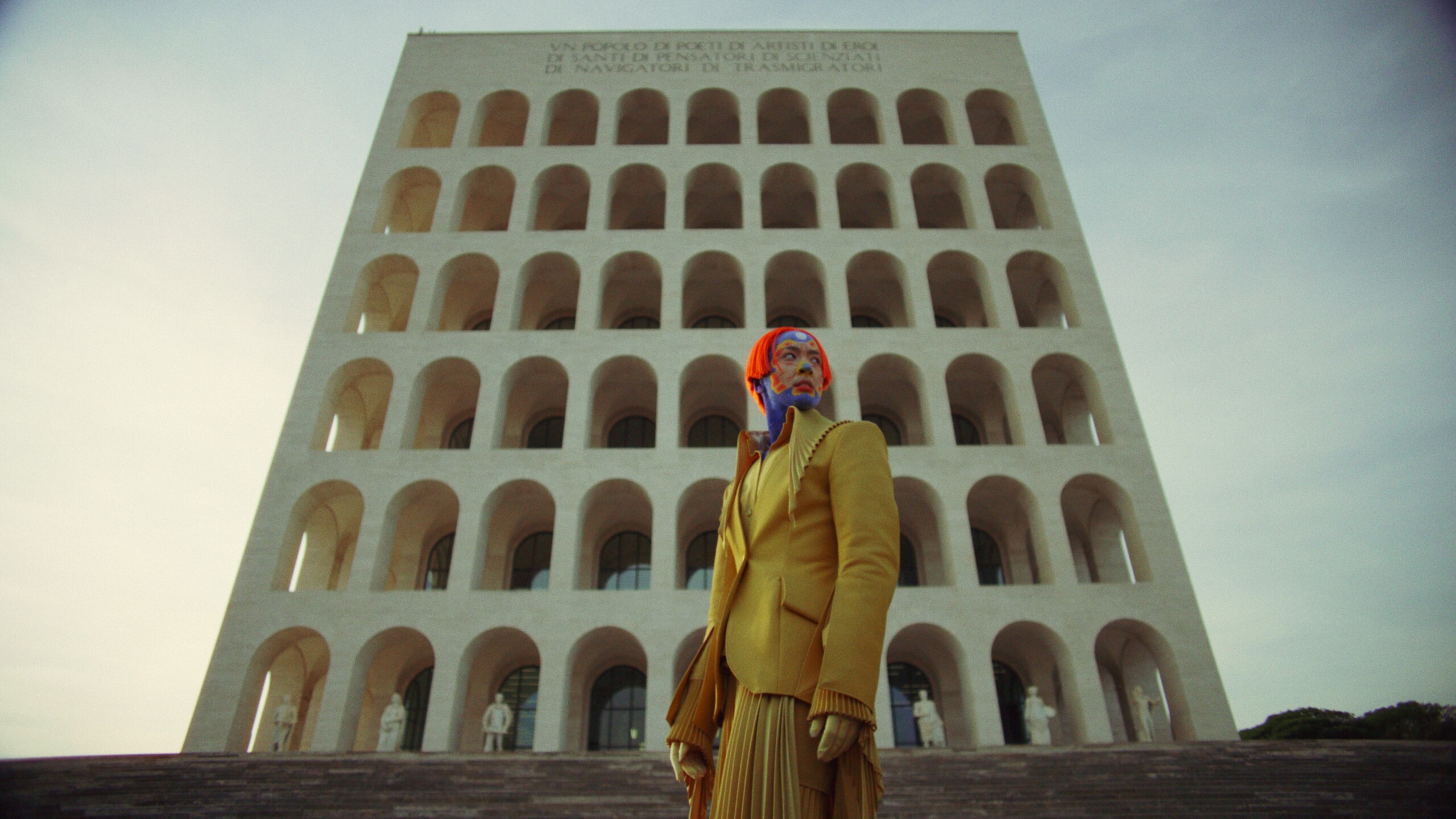 Person i gul kostym framför ett romerskt höghus