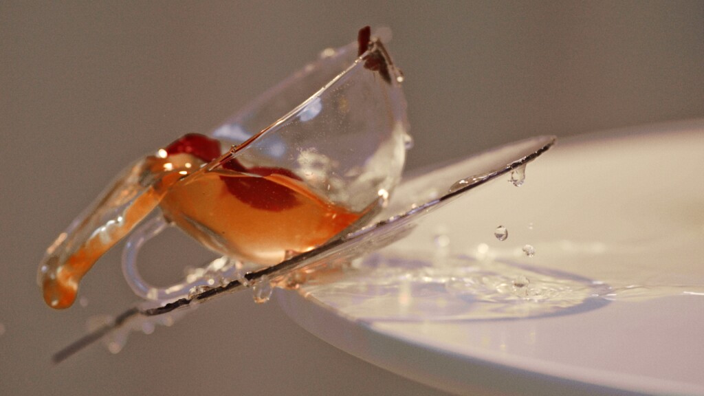 Glass cup with tea falling from white table 