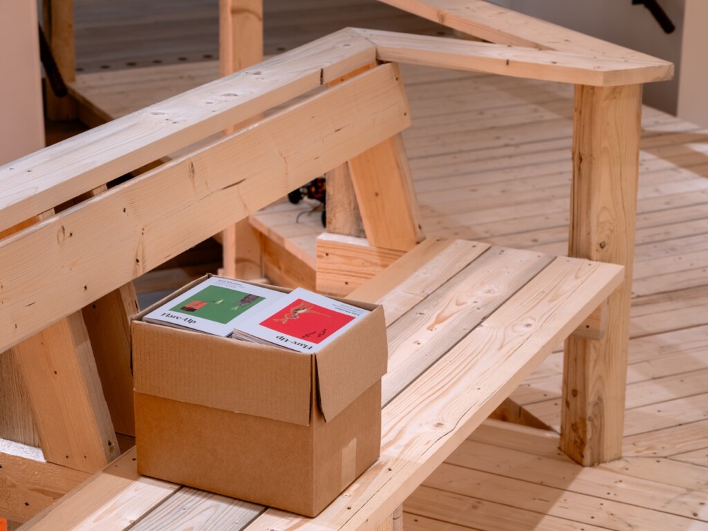 Box of red and green booklets written by Katie Kitamura on a wooden bench