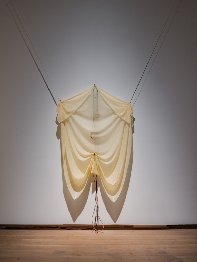 Wall-mounted draped latex sculpture in light yellow.