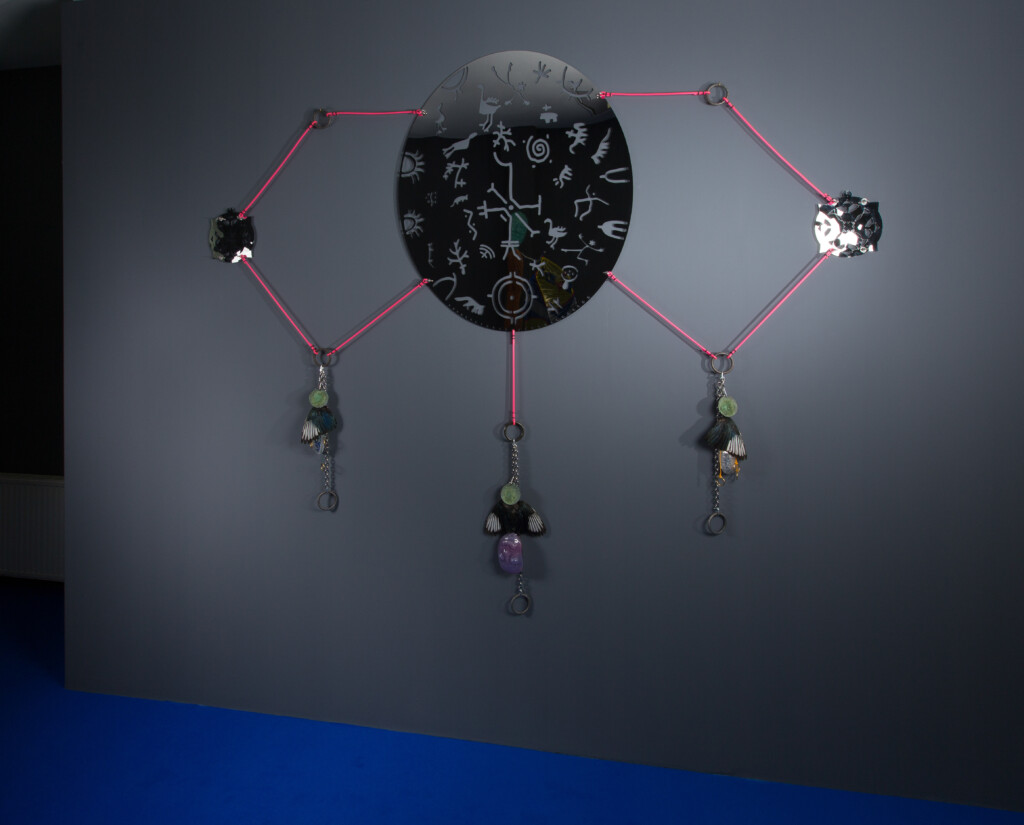 Väggskulptur av Olof Marsja av syntetiskt rep, skatvingar, glas, stål, kedja i rostfritt stål, mässing, lyftögla och speglad plåt i rostfritt stål.